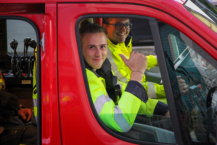 Zwei Feuerwehrmänner winken aus dem Verkehrsdienst-Fahrzeug