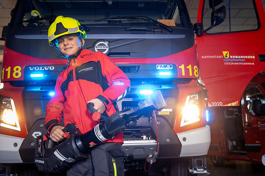 Ein Jugendfeuerwehler posiert mit dem Spreizer vor einem Feuerwehrfahrzeug